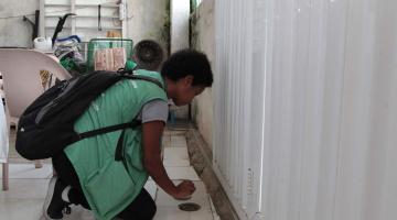 Agente de combate à dengue está agachada observando ralo. #Paratodosverem