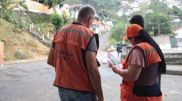 Agentes da Defesa Civil uniformizados e reunidos em rua de morro. #Pracegover