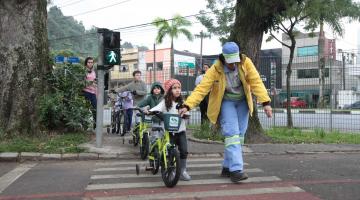 agente ajuda crianças a atravessarem a rua com bicicletas #pracegover 