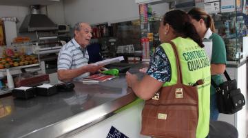 Agentes da Ouvidoria estão de costas para a foto e em frete a um balcão. Elas conversam com um homem atrás do balcão. #Pracegover