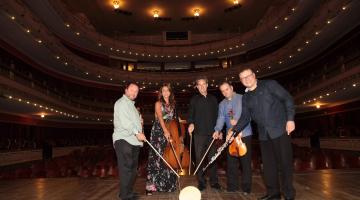 membros do quarteto estão com baquetas unidas em palco #pracegover 