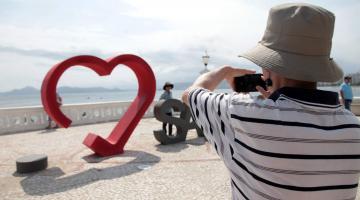 Homem fotografa letreiro com a palavra santos e coração #pracegover 