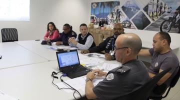 Pessoas reunidas em torno de uma mesa, com um quadro ao fundo. #Pracegover