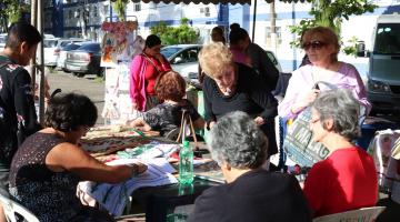 senhoras estão em mesa com bordados #pracegover 