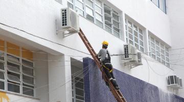 Homem em escada trabalha em parede de escola #pracegover 