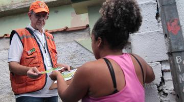 técnico da defesa civil entrega panfleto a mulher #pracegover 