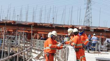 Construção do viaduto Piratininga. Homens estão trabalhando sobre trecho do viaduto. Eles estão próximos a um longo guarda-corpo. Estão visíveis estruturas metálicas. #Pracegover