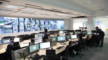 Centro de controle operacional com vários computadores e várias telas com imagens das câmeras. #paratodosverem