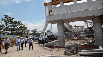 Várias pessoas estão caminhando e observando estrutura de concreto de futura ponte. #Pracegover