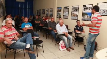 Alunos sentados em sala olham professor durante explicação #pracegover 