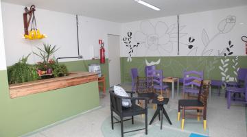 Sala com mobiliário de material reaproveitado. Há cadeira, luminária, pintura na parede, assentos nas cadeiras e outros objetos. #Paratodosverem