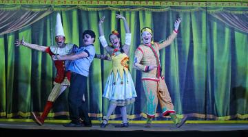 QUATRO ATORES VESTIDOS DE PALHAÇOS ESTÃO NO PALCO. CORTINA AO FUNDO. NO ALTO SE LÊ TEATRO A BORDO. #PARATODOSVEREM