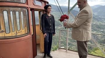 homem dá flor para mulher com teleférico atrás