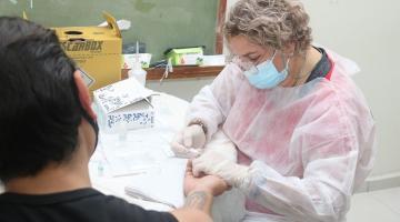 mulher faz teste de HIV/sífilis em homem que está de costas para a foto. O exame é feito com a retirada de uma gota de sangue do dedo. #paratodosverem
