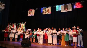 Homenageadas em cima do palco com flores #paratodosverem