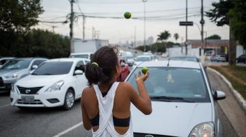 menina de costas para a foto faz malabares com limões na avenida diante de carros. #paratodosverem