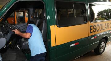 Homem está de costas na entrada do motorista de uma perua escolar. #Paratodosverem