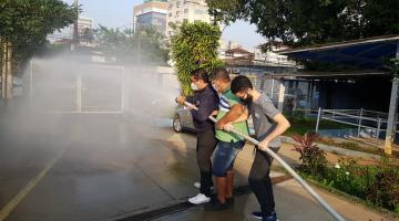 três pessoas seguram mangueira de combate a incêndio que está lançando água. #paratodosverem