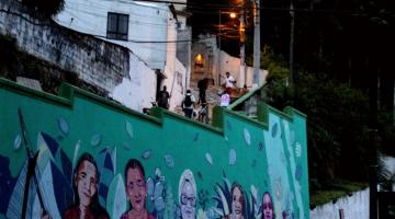 MURO ILUSTRADO NO SOPÉ DO MONTE SERRTA COM A ESCADARIA NO ALTO E PESSOAS CIRCULANDO. #PARATODOSVEREM