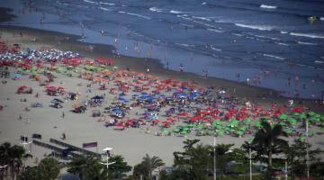 Vista aérea de praia com vários guarda sois abertos. #paratodosverem