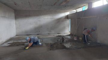 homens trabalham na aplicação de contrapiso em sala. #paratodosverem