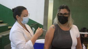 Mulher recebe aplicação de vacina no braço, feita por profissional de saúde. #pracegover