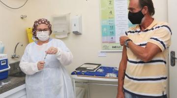 mulher prepara vacina enquanto homem levanta manga de camiseta para ser imunizado. #paratodosverem