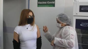 Jovem recebe aplicação de vacina por profissional de saúde paramentada. #pracegover