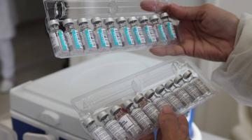 mãos seguram caixa transparente com vários tubos de vacina. #paratodosverem