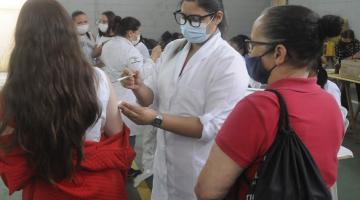 mulher vacina menina que está de costas para a foto. Outra mulher observa. #paratodosverem