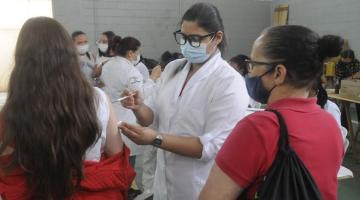 enfermeira aplica vacina em jovem e mulher mais velha acompanha ao lado #paratodosverem