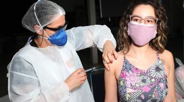 mulher usando avental, máscara e gorro vacina outra mulher. #paratodosverem
