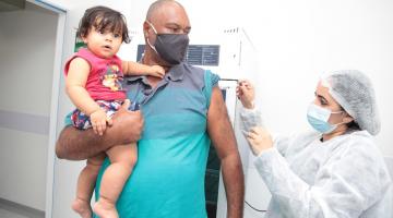 homem é vacinado. Ele segura um bebê nos braços. #paratrodosverem
