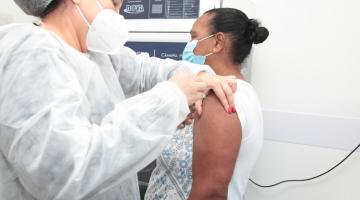 mulher usando avental touca e máscara injeta agulha em braço de outra mulher. #paratodosverem