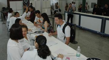 balção de atendimento montado em salão, com atendentes de um lado e turistas de outro. Sobre o balcão há papéis. #paratodosverem