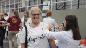 Mulher com camisa branca escrita Desperte recebe vacinação de profissional de saúde. #pratodosverem