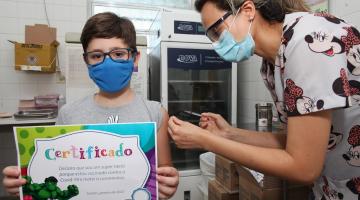criança recebe vacina segurando um certificado #paratodosverem