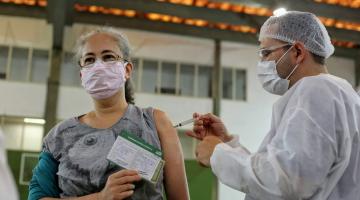 enfermeiro aplica vacina em mulher que segura carteirinha #paratodosverem
