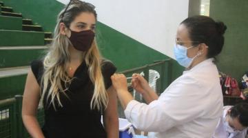 Mulher é vacina por profissional de saúde em ginásio poliesportivo. #pracegover