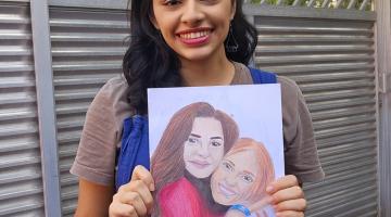 mulher sorri para a foto segurando um desenho. #paratodosverem 