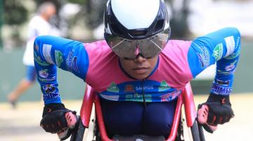 Paratleta, de óculos e capacete, corre em cadeira de rodas. #paratodosverem