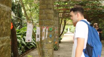 homem lê poesia em varal na entrada do orquidário. #paratodosverem