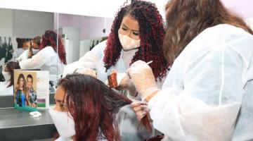 duas mulheres fazem pintura em cabelo de outra mulher #paratodosverem