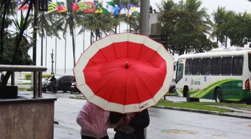 duas mulheres estão sob guarda-chuva que está envergado devido ao vento. #paratodosverem