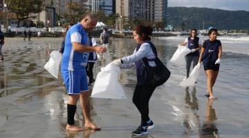 jovens estão na beira do mar segurando sacos de lixo onde depositam material coletado. #paratodosverem