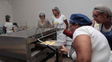 Mulheres colocam alimento no forno industrial. #pracegover