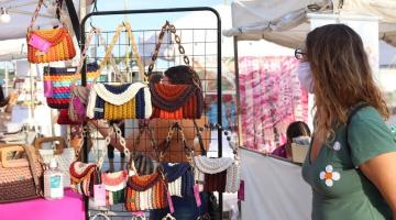 bolsas de crochê penduradas em araras. Mulher está olhando os produtos. #paratodosverem