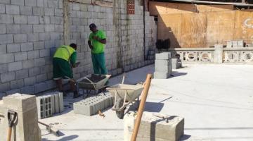 Operários empilham lajotas em obra de construção de parque infantil. #pracegover