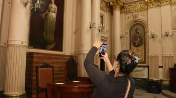 Mulher tira foto com o celular da imagem da Princesa Isabel. #pracegover