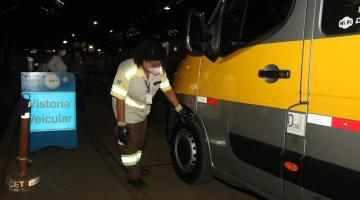 mulher usando uniforme com faixas reflexivas observa pneu frontal de van escolar. #paratodosverem